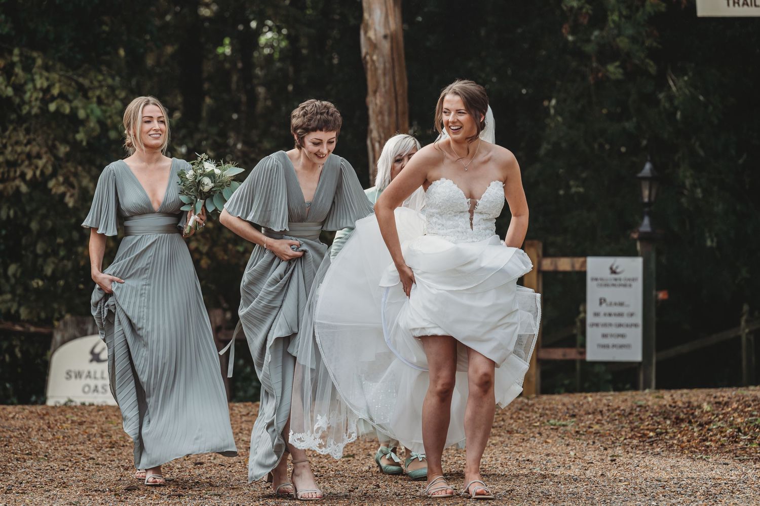 Three people joyfully walking outdoors, with one in a white wedding dress lifting the skirt while walking.