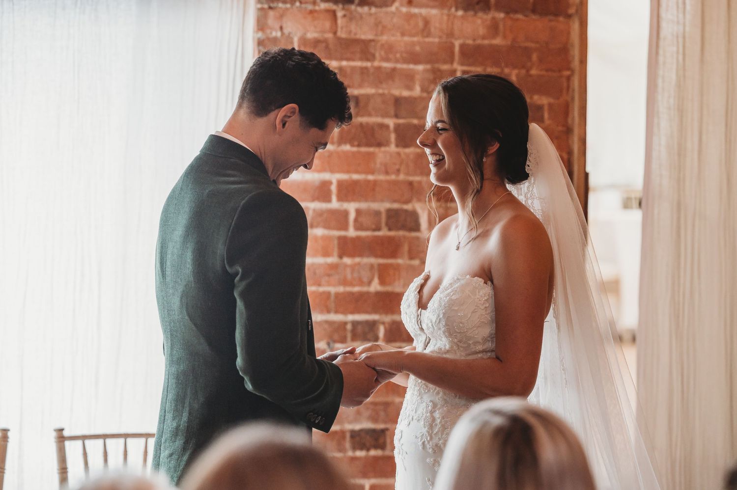 A tender moment during a wedding ceremony as the couple exchanges rings in front of an exposed brick wall.