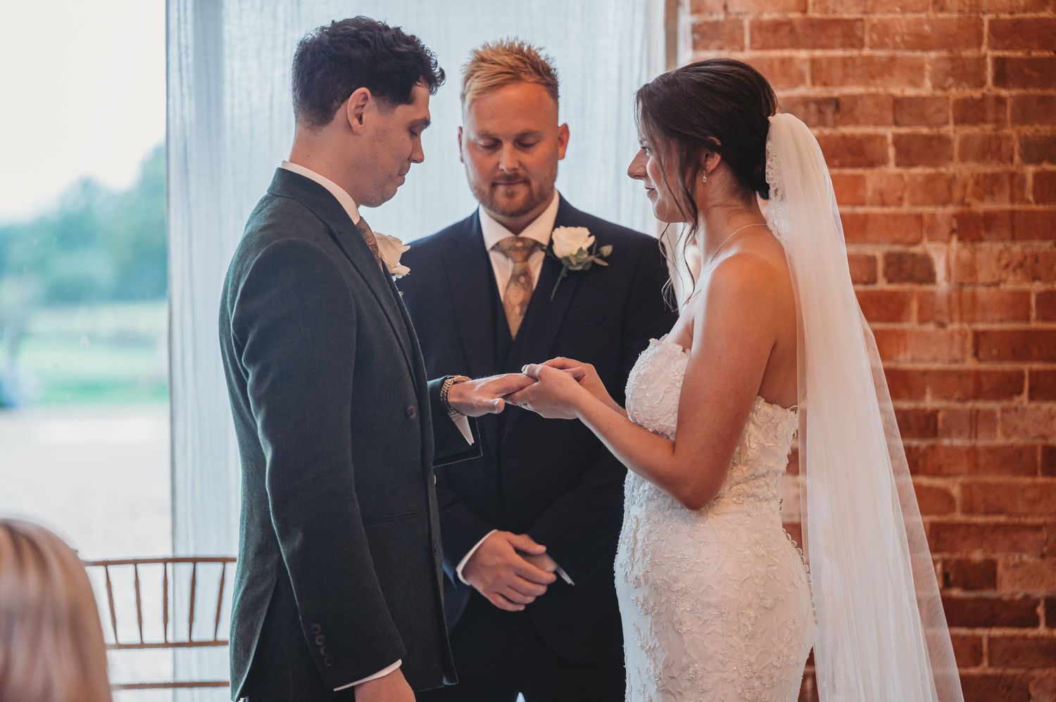 A wedding ring exchange ceremony in front of exposed brick walls with natural lighting.