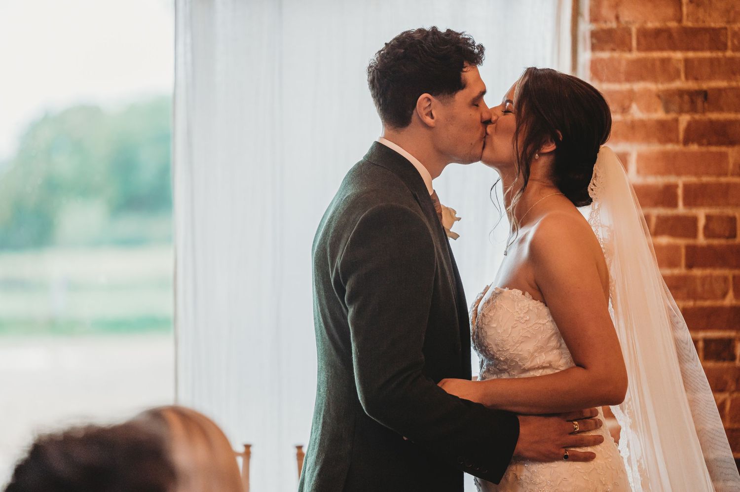 A tender wedding ceremony kiss moment against a backdrop of exposed brick walls.