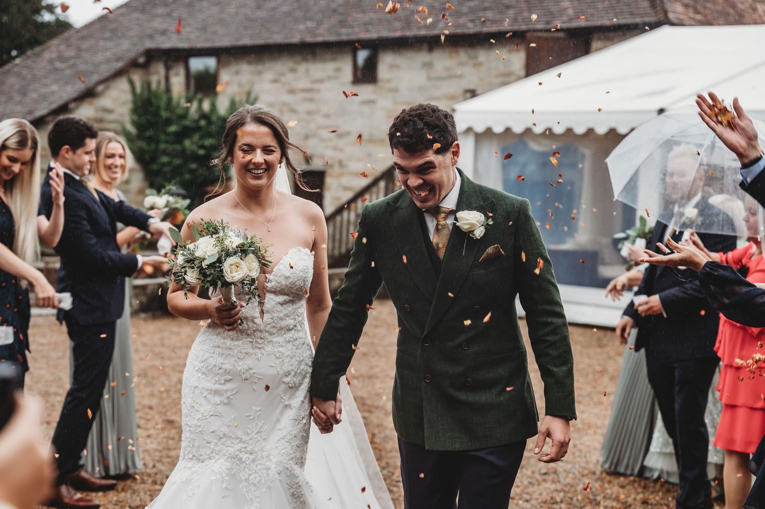 Wedding celebration with couple walking through confetti while guests cheer at rustic venue.