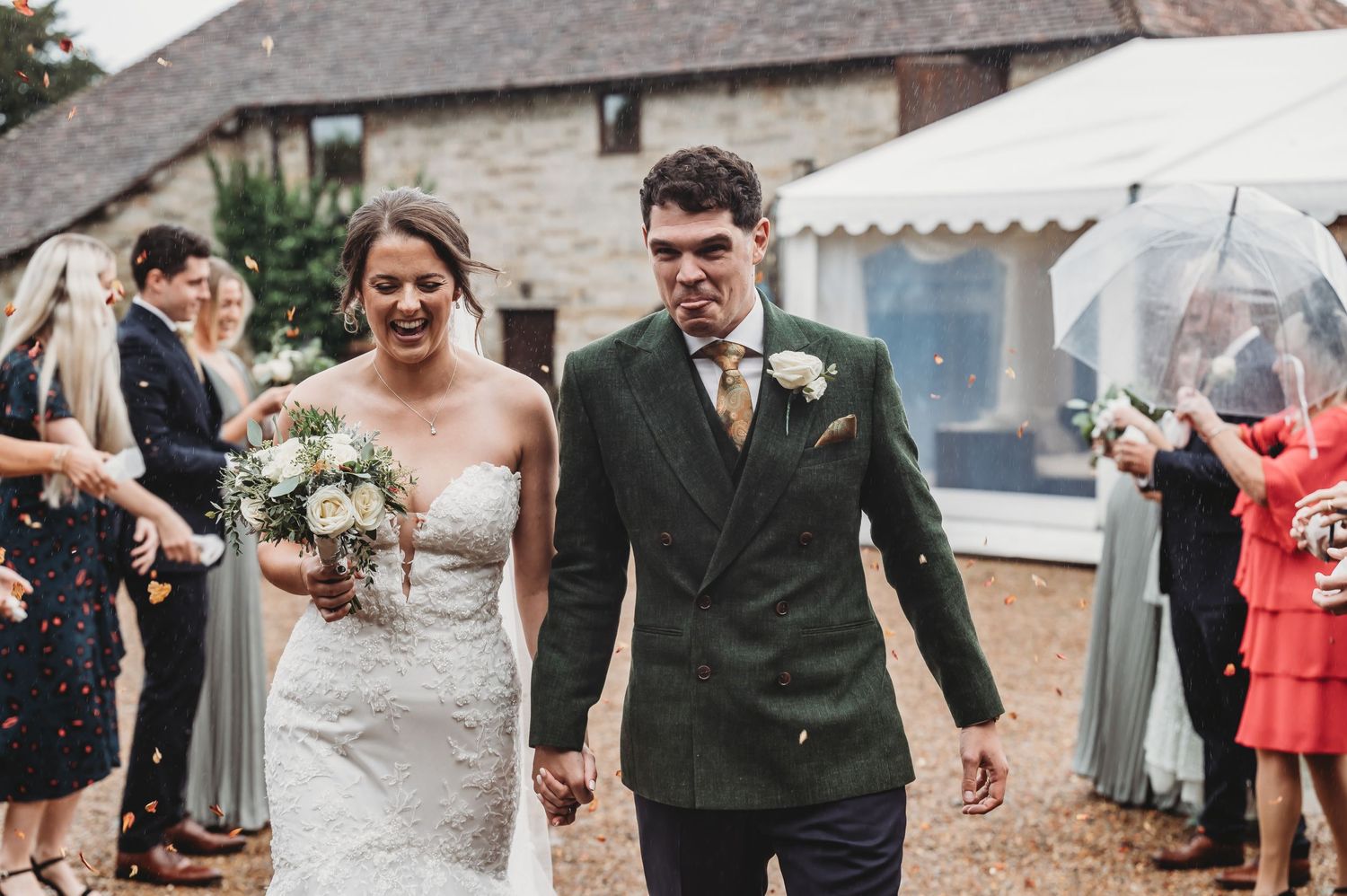 Elegant couple celebrates their wedding day outside a rustic venue with guests looking on.