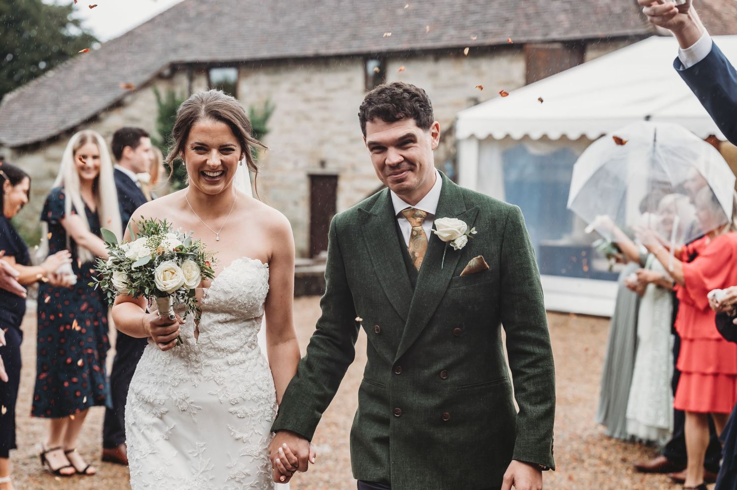 Happy couple exits their wedding ceremony while guests celebrate at a countryside venue.