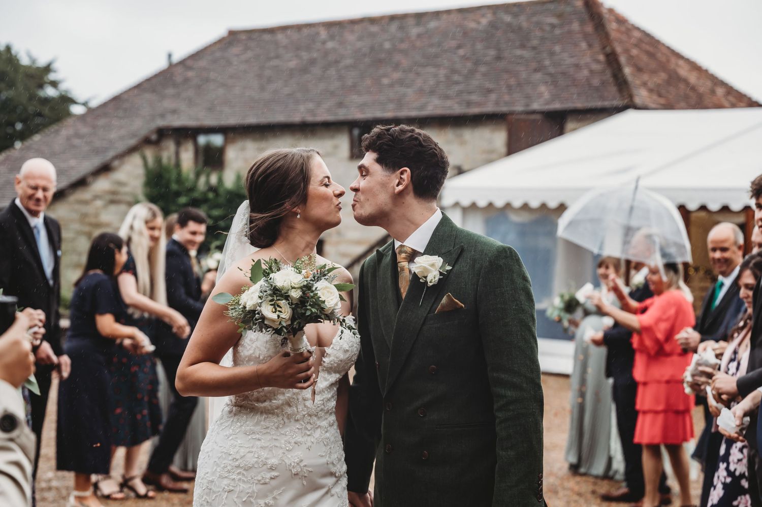 Newlyweds embrace during their celebration outside a traditional stone venue with guests looking on.