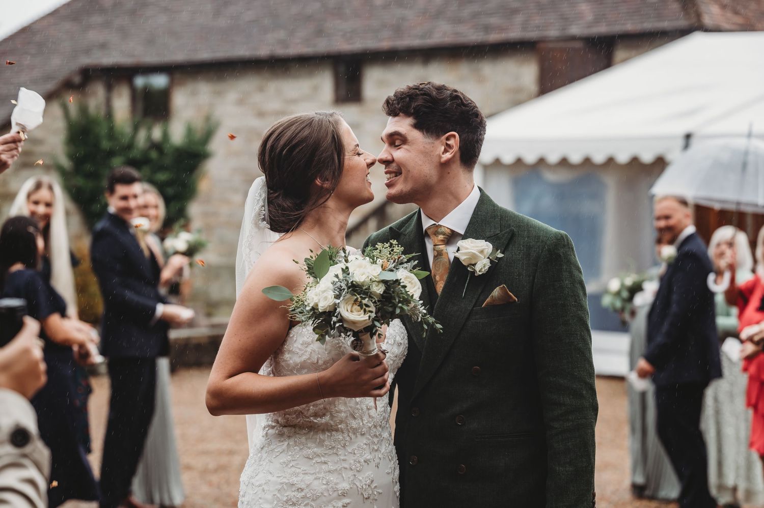 A wedding celebration outside a rustic venue with guests watching the happy couple.
