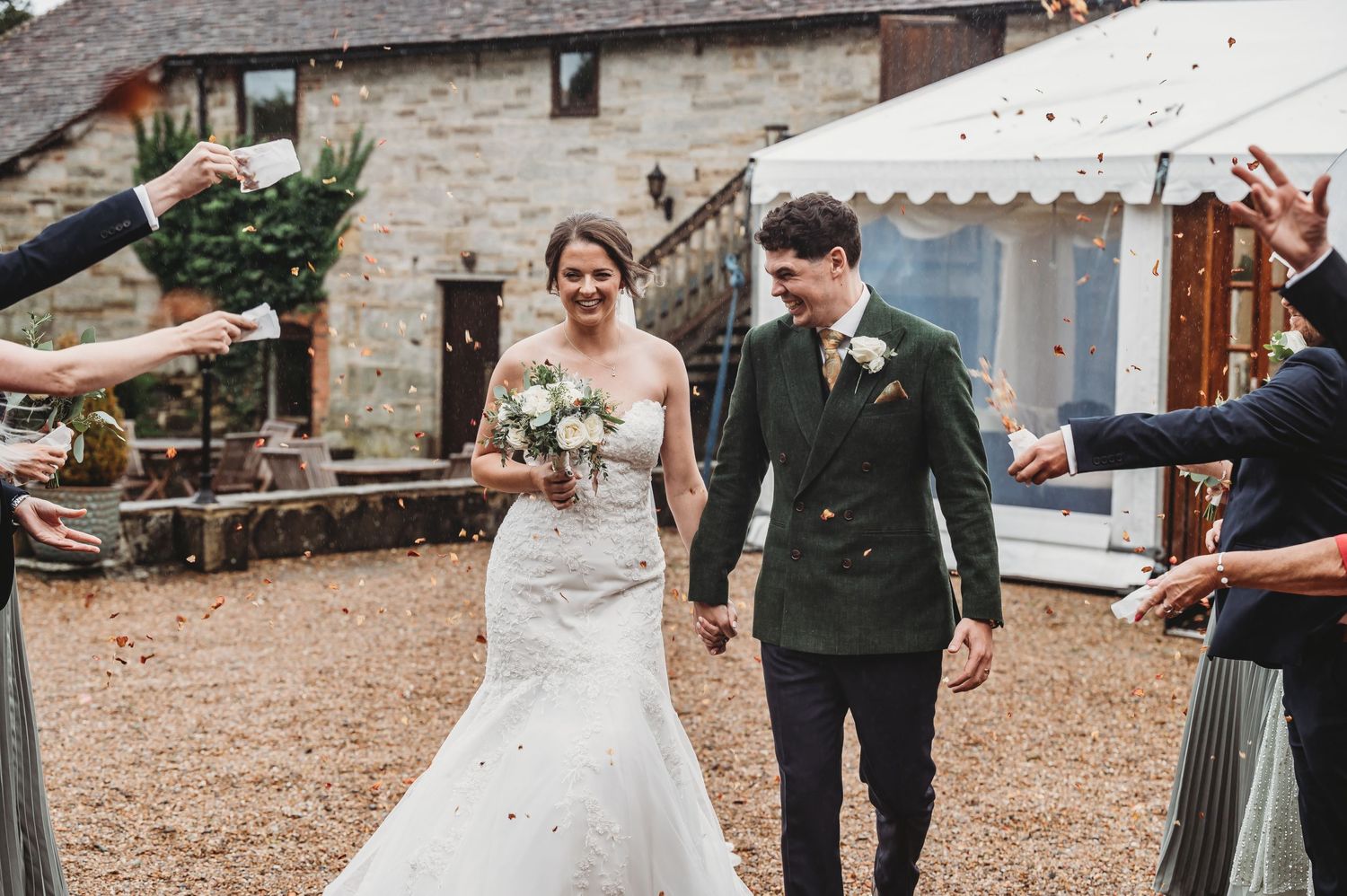 A couple celebrates their wedding day walking past guests outside a rustic venue with white tent.