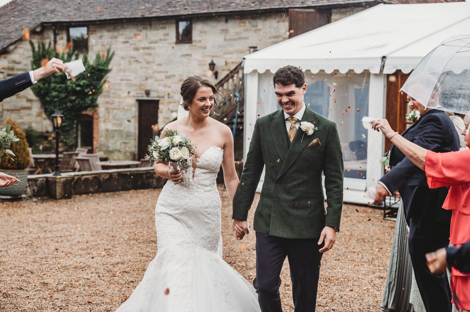 A couple celebrates their wedding day walking hand in hand past guests outside a stone building.