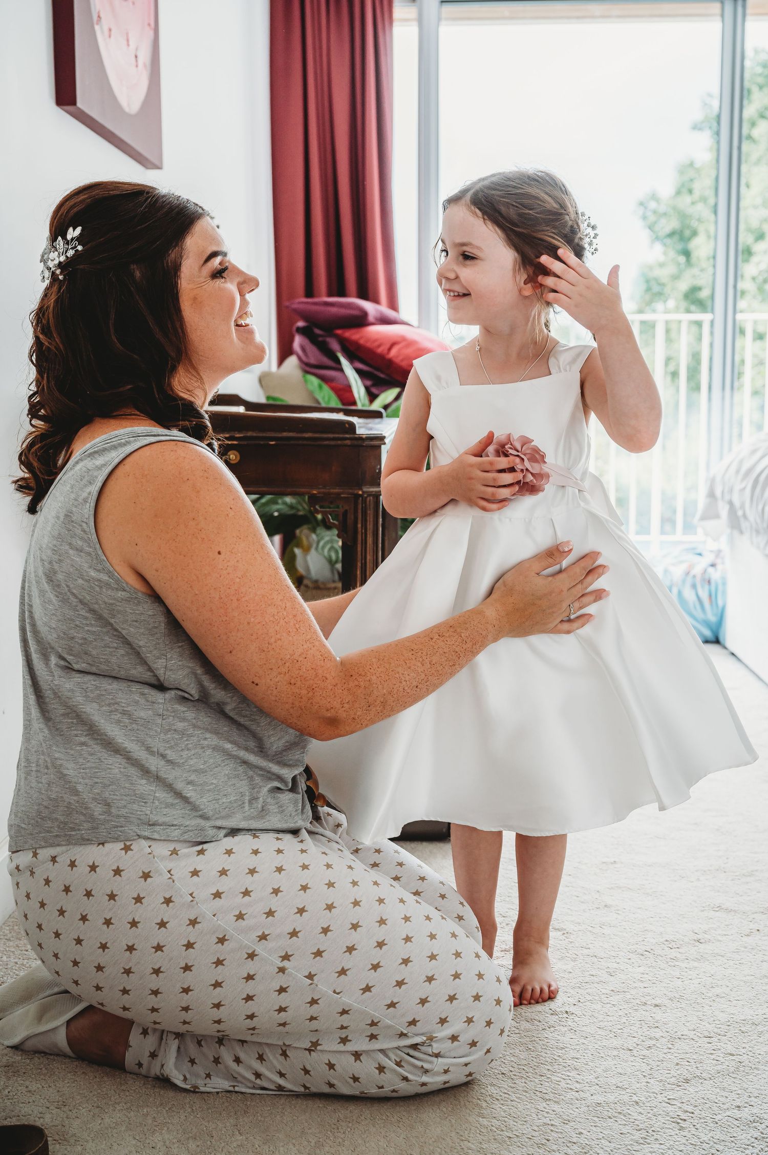 A tender moment shared between two people in a bedroom, with one sitting on carpet and another wearing a white dress.