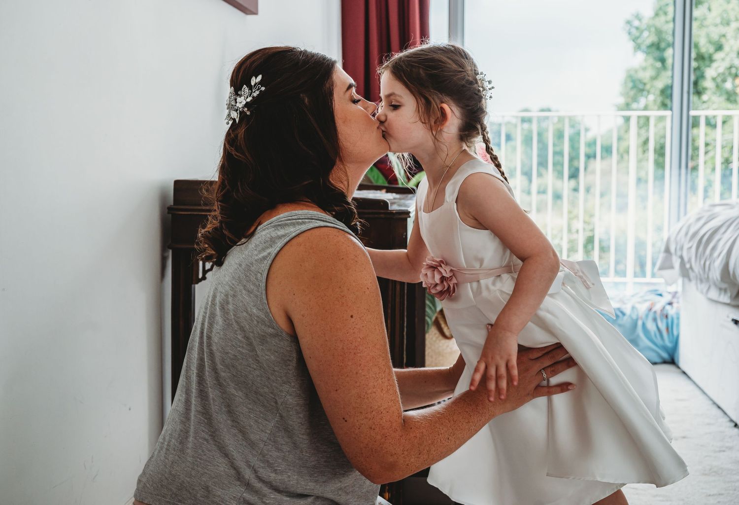 Sweet moment captured between a flower girl in a white dress and a woman in grey.