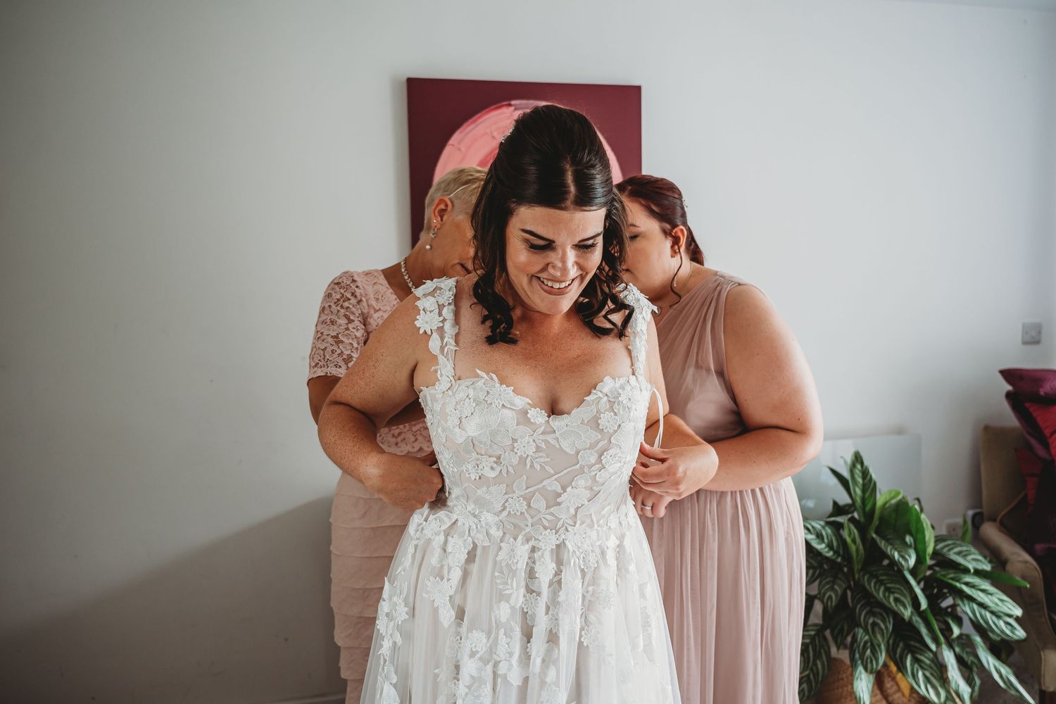 Someone wearing an elegant lace wedding dress gets help with final preparations while getting ready for their big day.