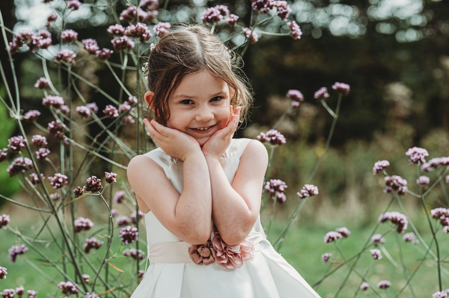 White dress and flower corsage surrounded by delicate purple wildflowers in a dreamy outdoor garden setting.