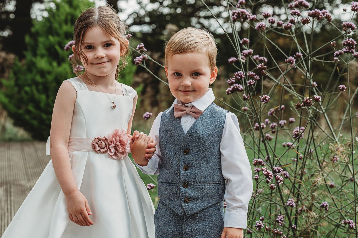 Children in formal attire standing together at an outdoor garden setting with wildflowers.