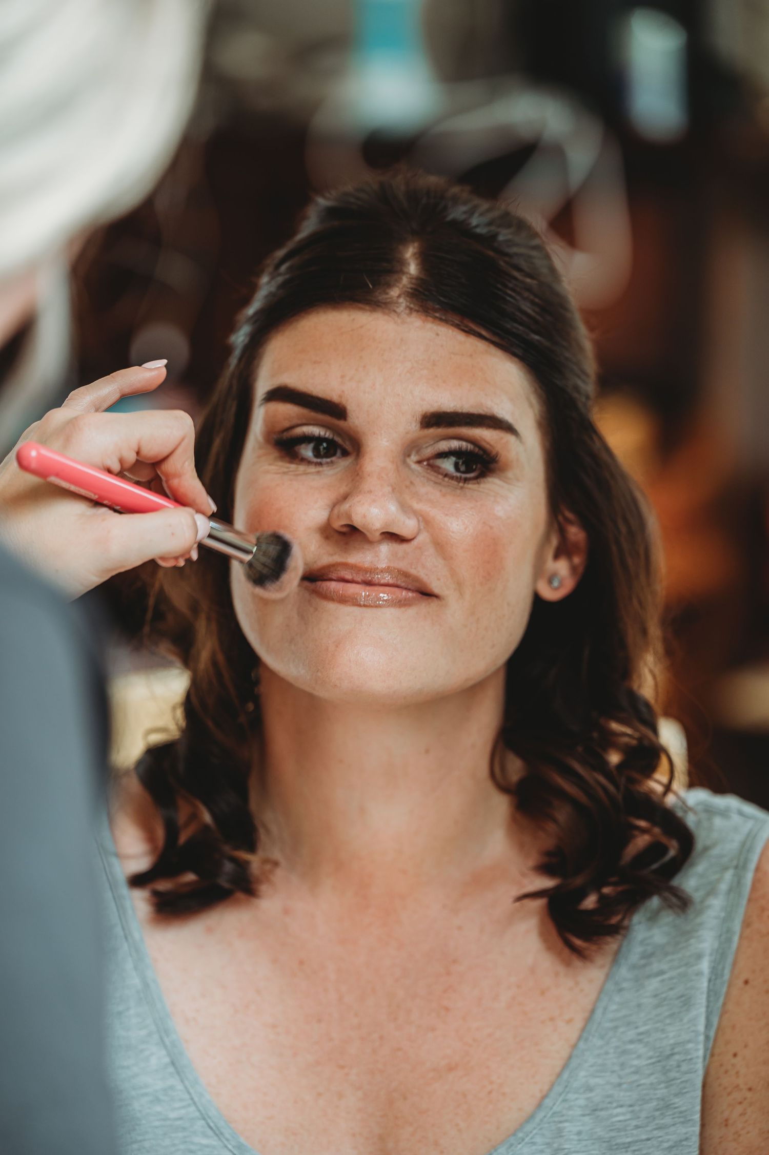 Makeup artist applies powder with pink brush during professional beauty session in warm lighting.