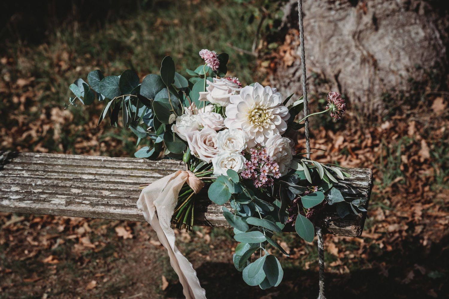 Rustic wedding bouquet with white dahlias and eucalyptus leaves resting on a wooden bench.