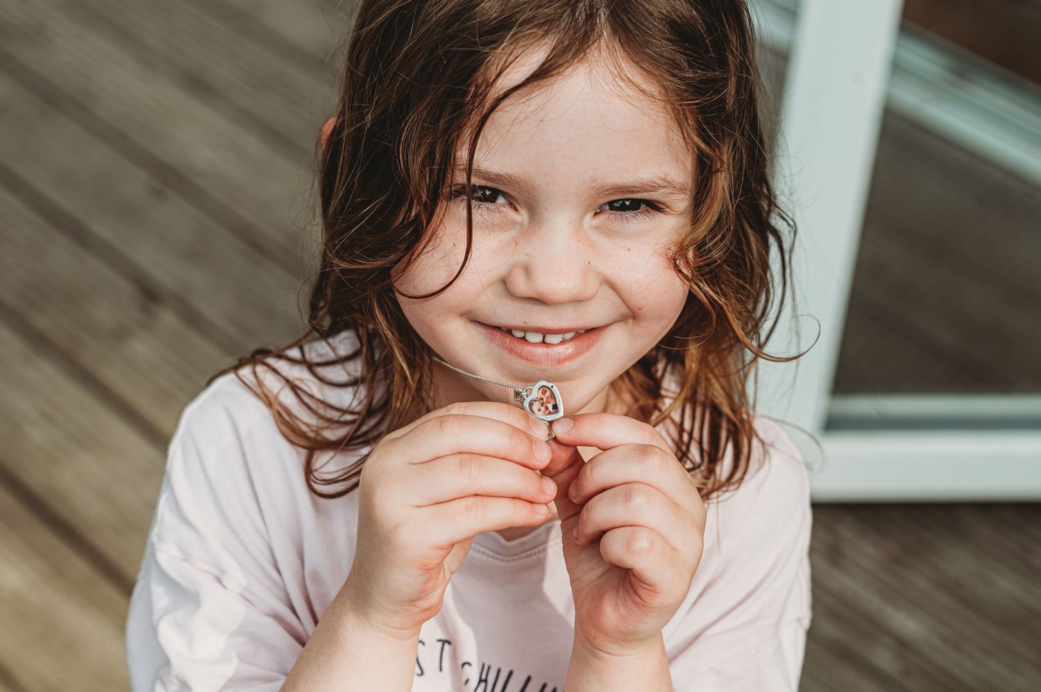 A young child with dark wavy hair and a white shirt smiles while holding something small.