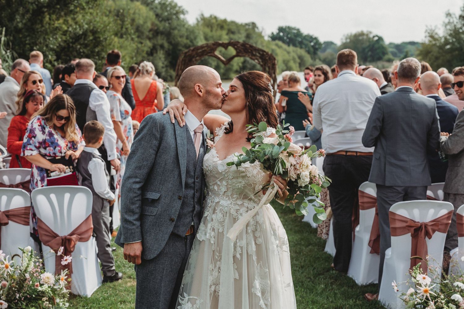 Romantic outdoor wedding celebration with guests gathered on lawn chairs during a summer garden ceremony.