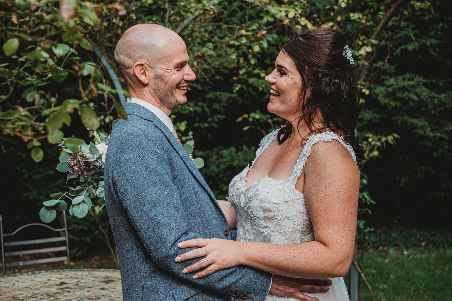 Joyful couple shares a candid moment together outdoors, with bride wearing lace dress and groom in gray suit.