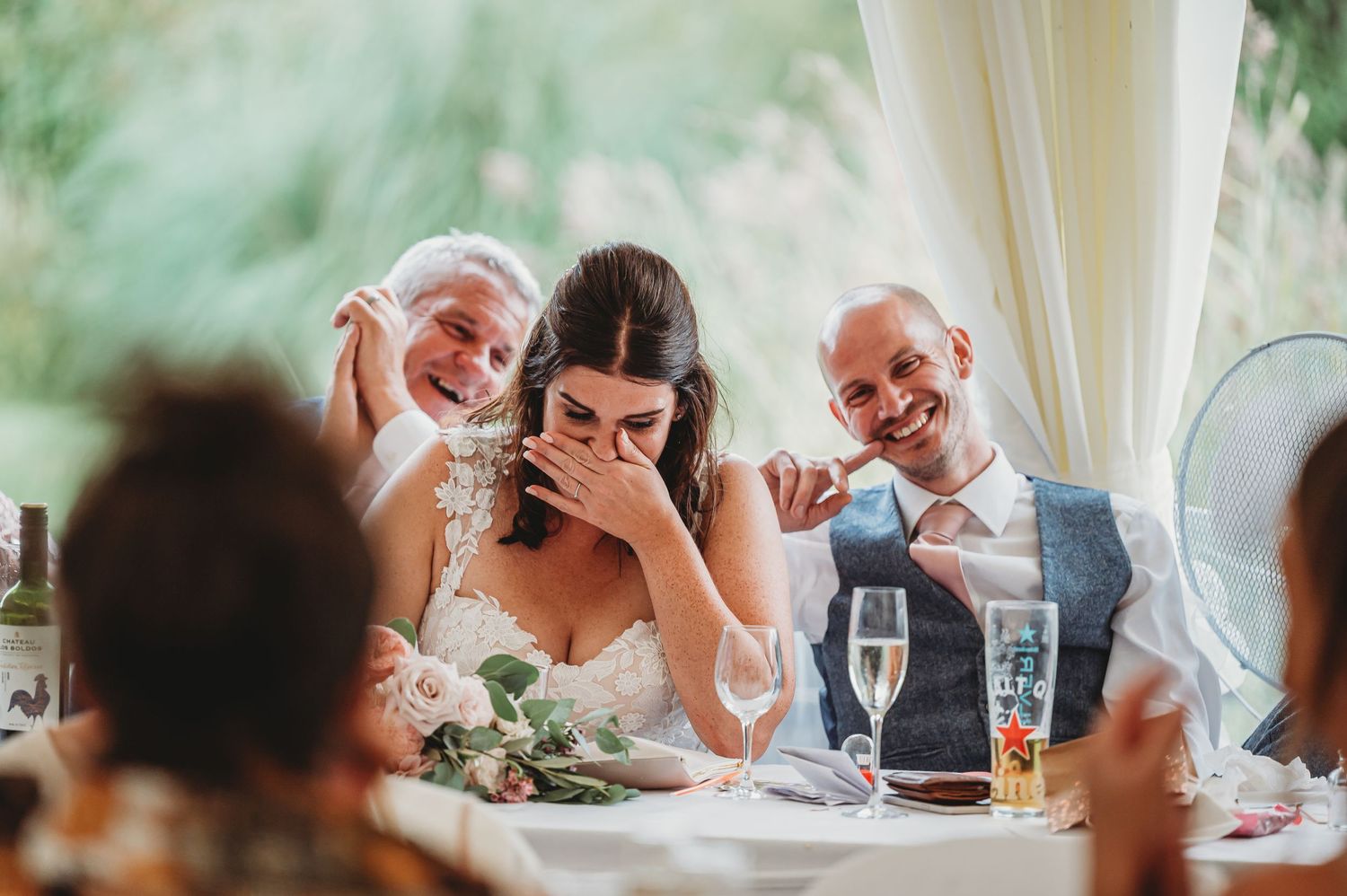 Candid moment of joyful laughter during wedding reception at head table with champagne glasses and floral decor.