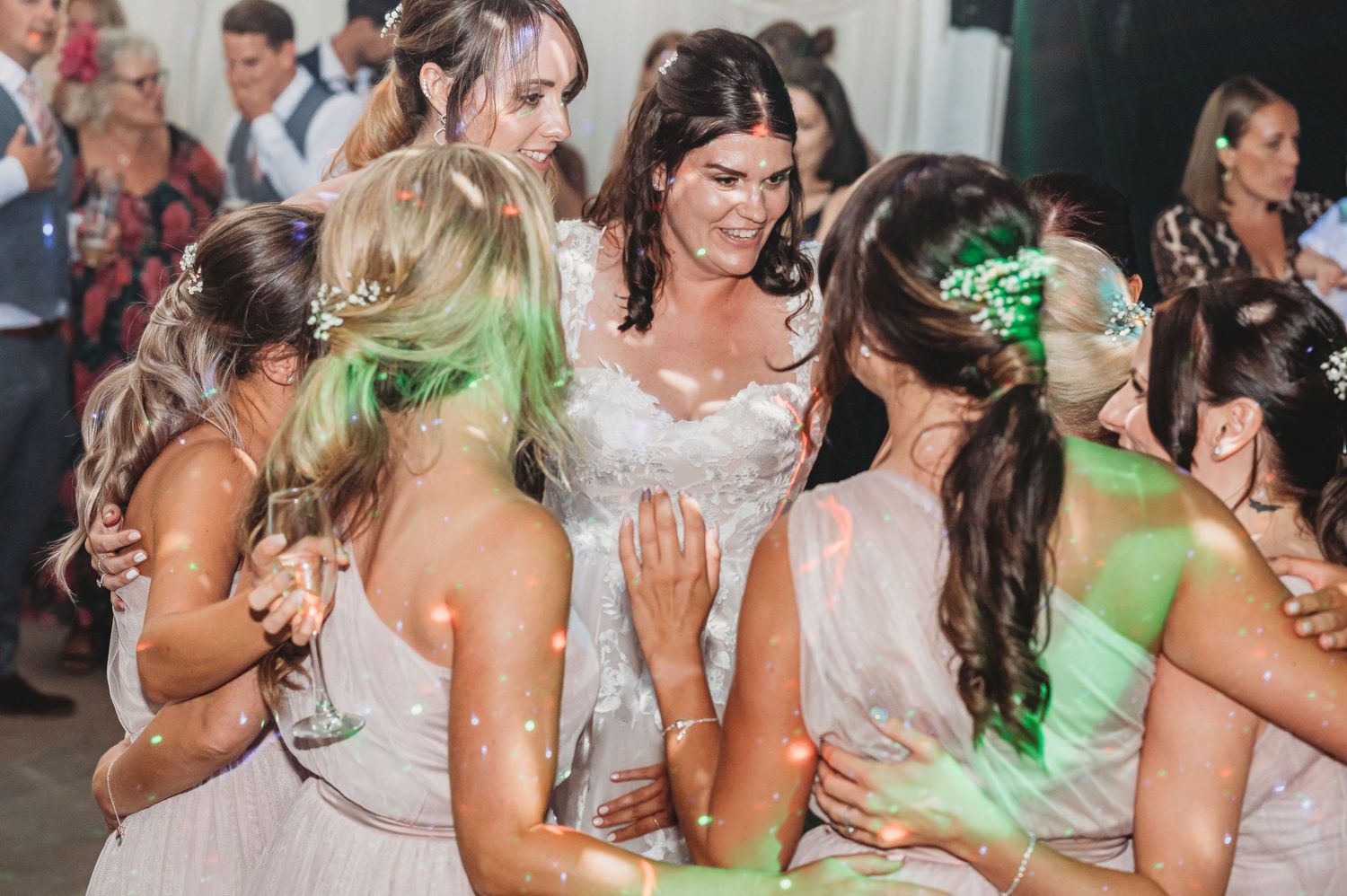 Wedding party attendees dancing together on the dance floor in light pink bridesmaid dresses under green party lighting.