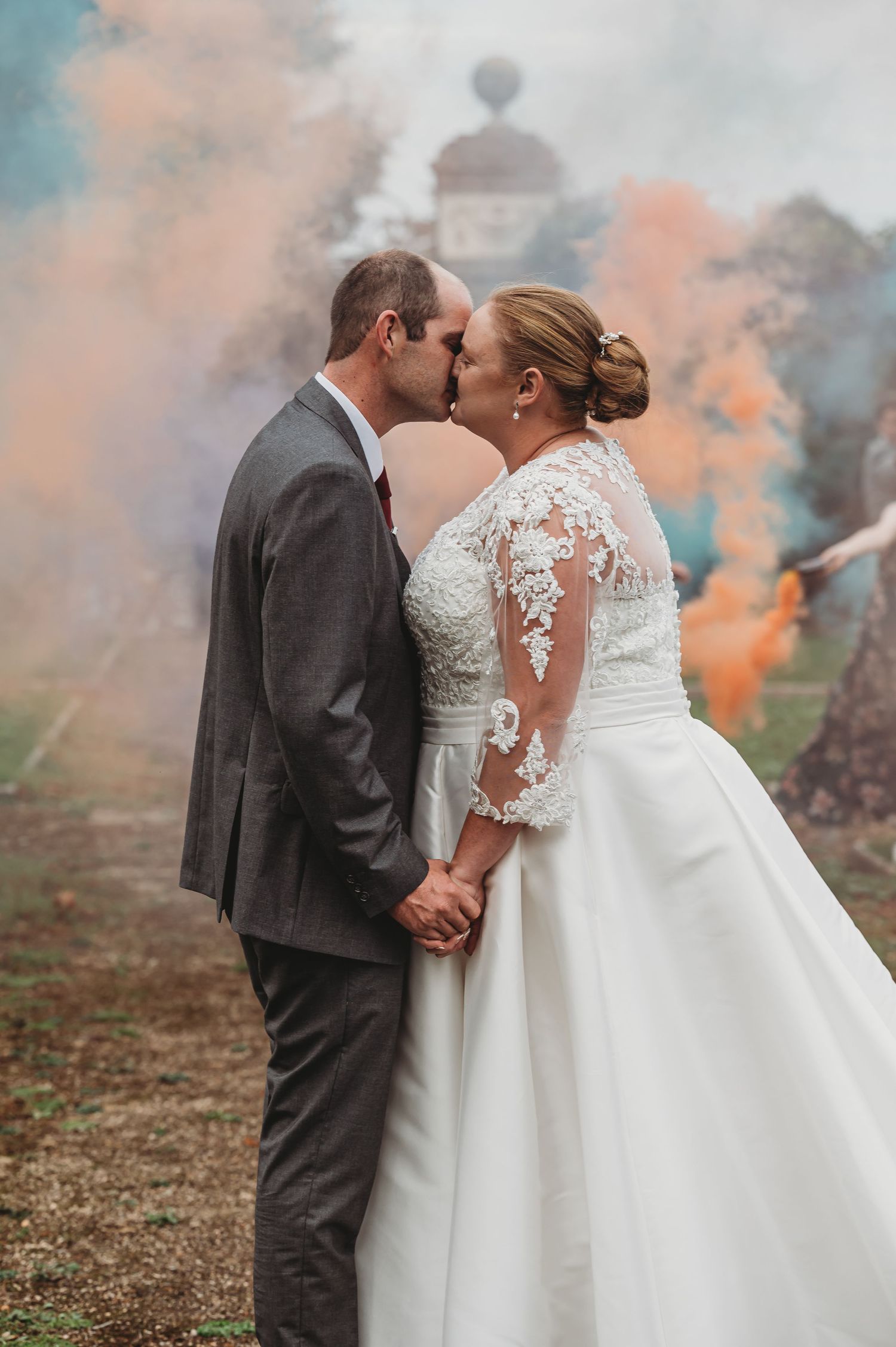 A romantic wedding photo with colorful smoke bombs creating a dreamy backdrop as a couple shares a tender kiss.