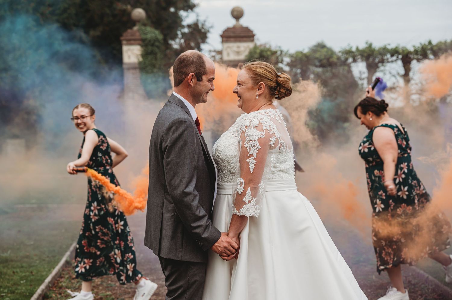 Newlyweds share romantic moment surrounded by colorful smoke bombs at outdoor wedding celebration.
