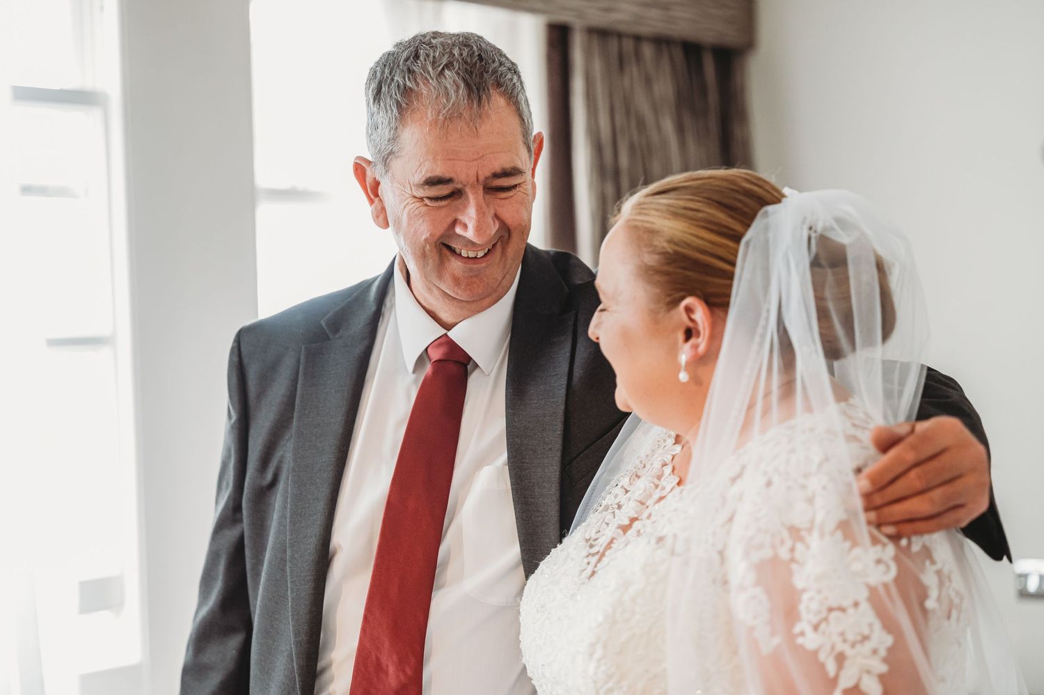 An emotional moment during a wedding as the bride in a white lace gown shares a tender moment with a man in a dark suit.