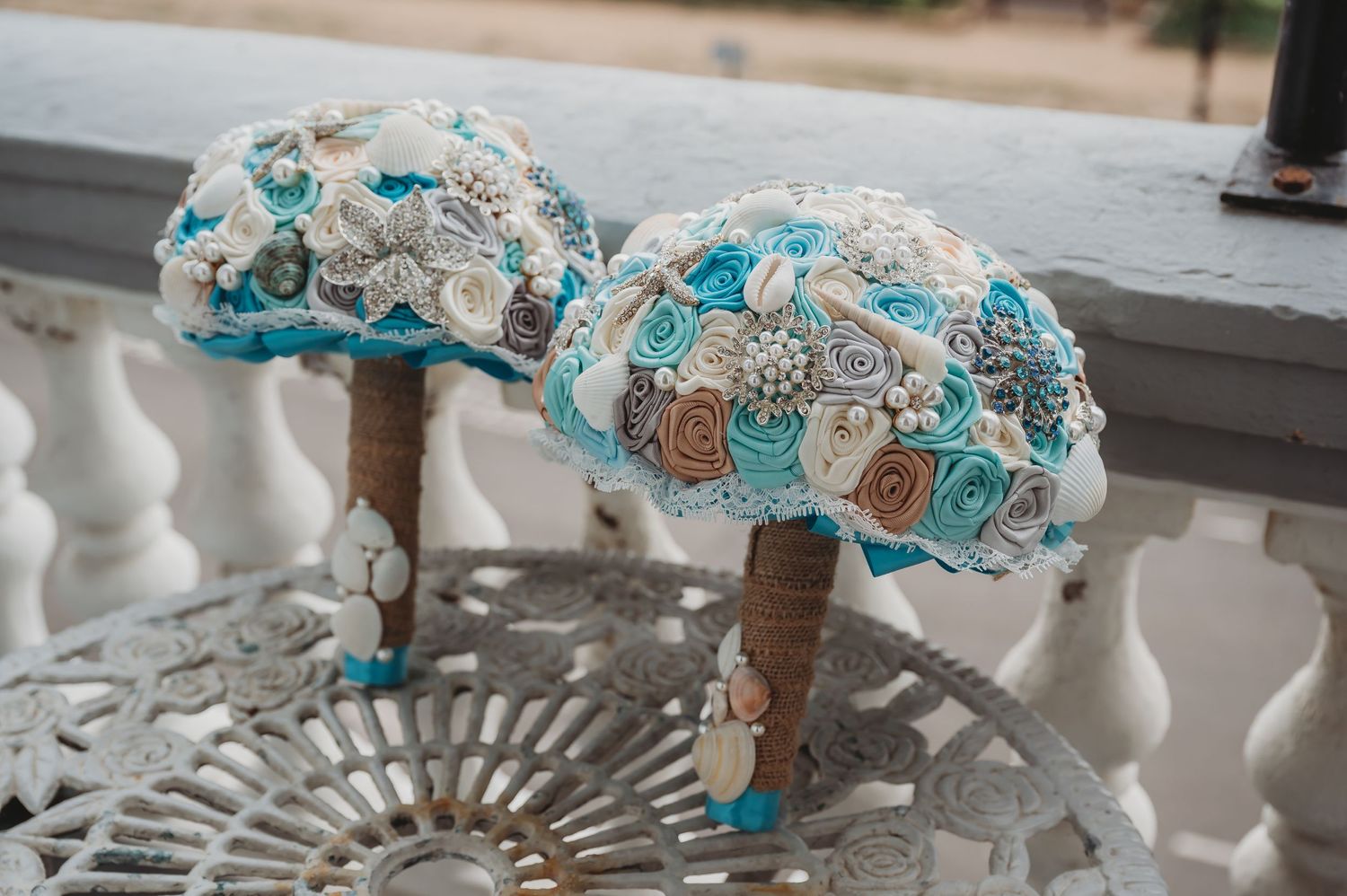 Two handmade wedding bouquets with turquoise and white fabric flowers and pearls rest on a decorative railing.