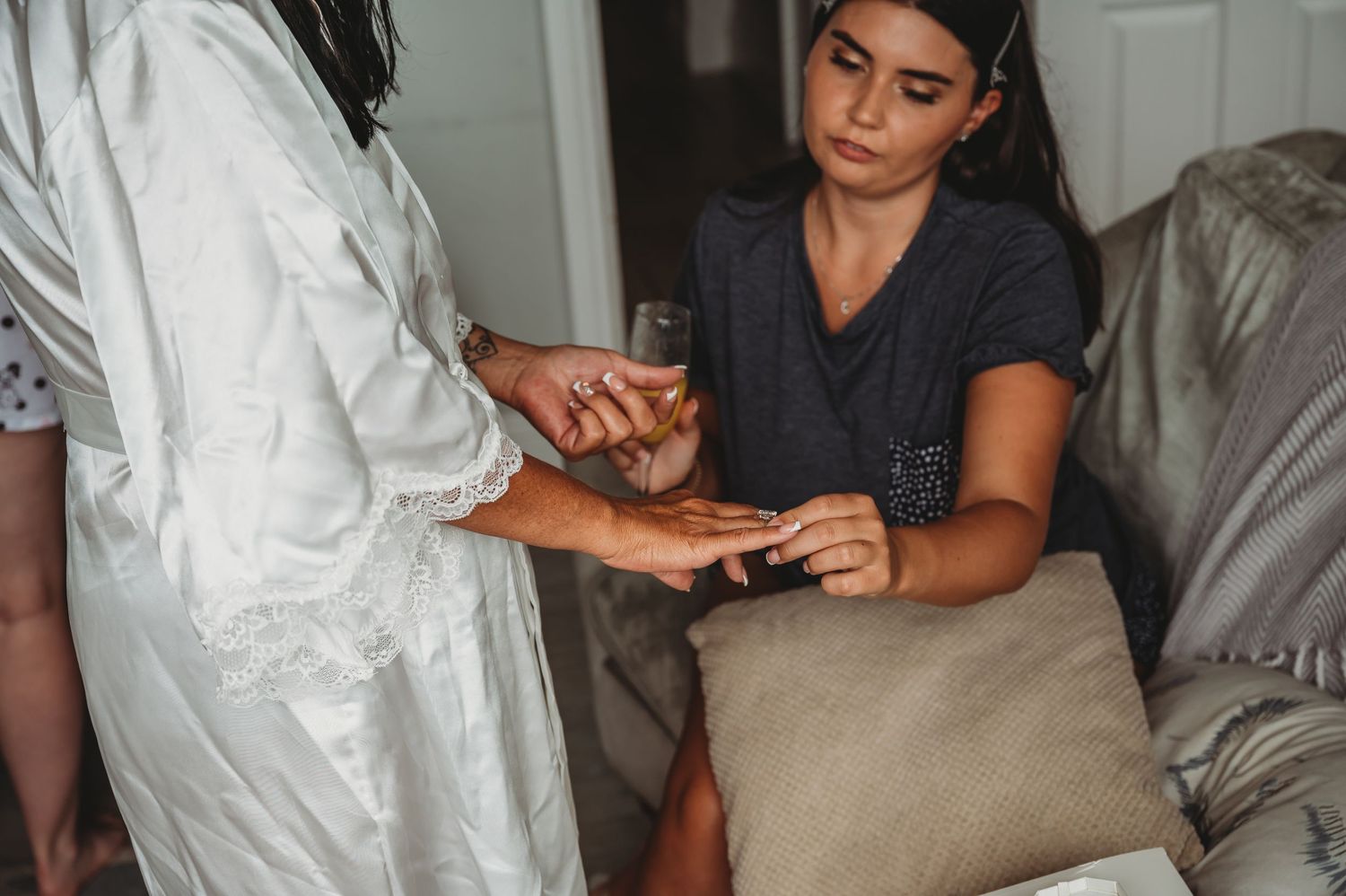 Professional nail technician wearing grey t-shirt provides manicure service to client sitting on beige couch in salon.