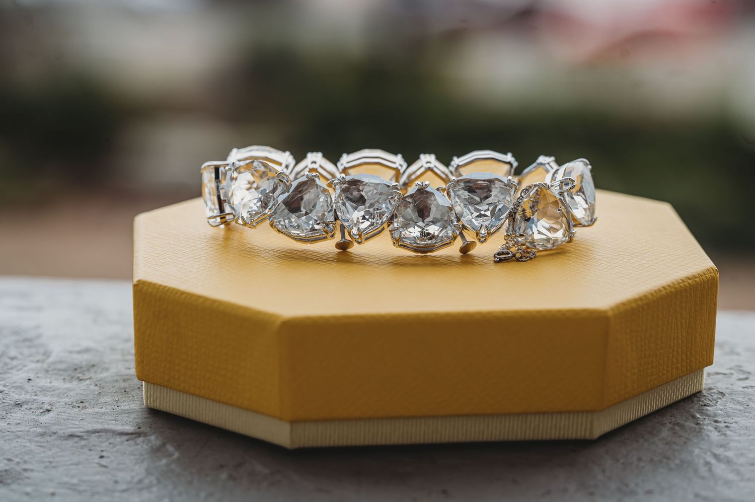 Elegant diamond wedding band displayed on gold hexagonal jewelry box with blurred background.