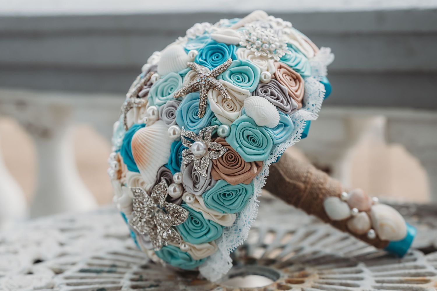 A stunning turquoise and beige brooch bouquet with crystal embellishments and satin roses on a lace background.