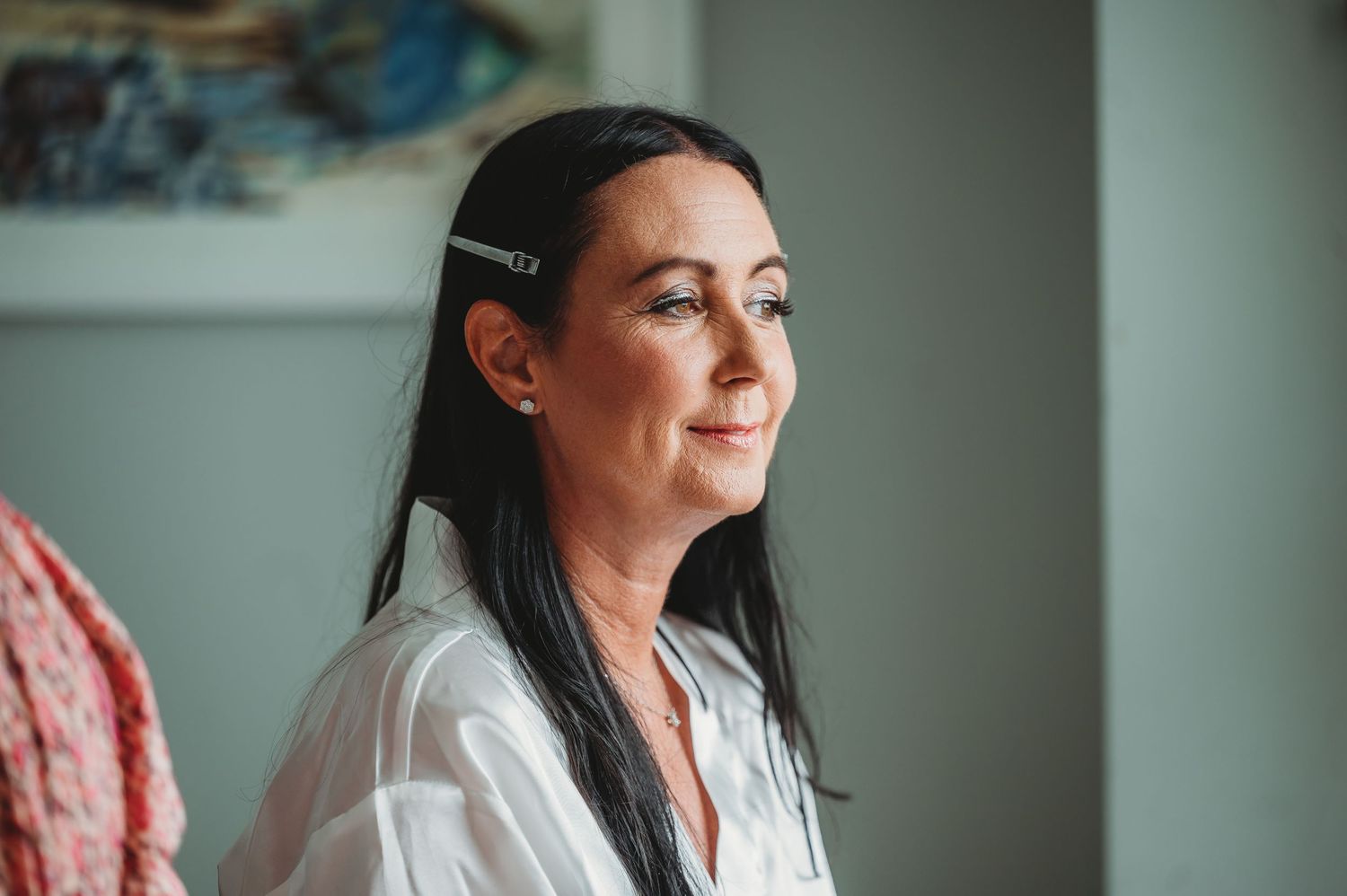 Profile view of someone with long dark hair wearing a white shirt looking towards window light with a soft contemplative expression.
