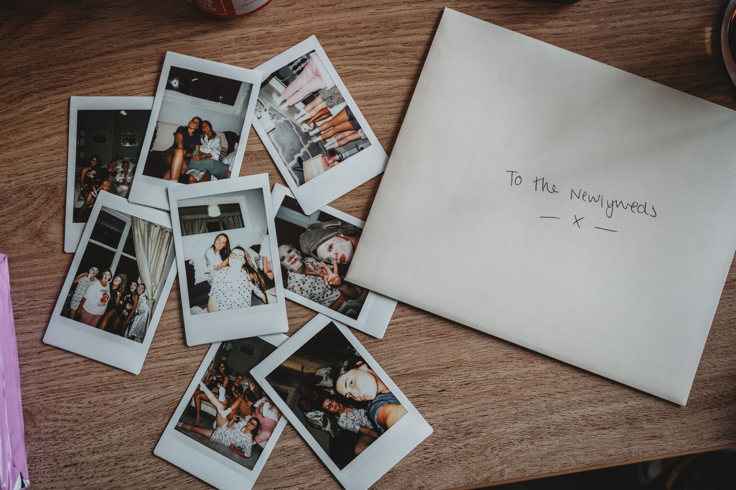 Collection of vintage polaroid photos spread on wooden surface next to white envelope on rustic table.