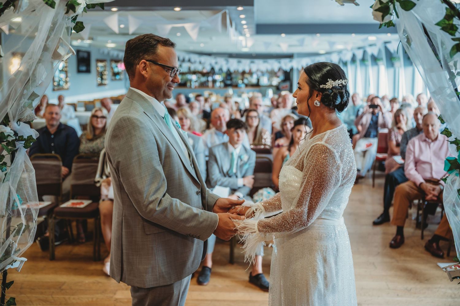 Two people share a special moment during their wedding ceremony in a rustic indoor venue filled with seated guests.