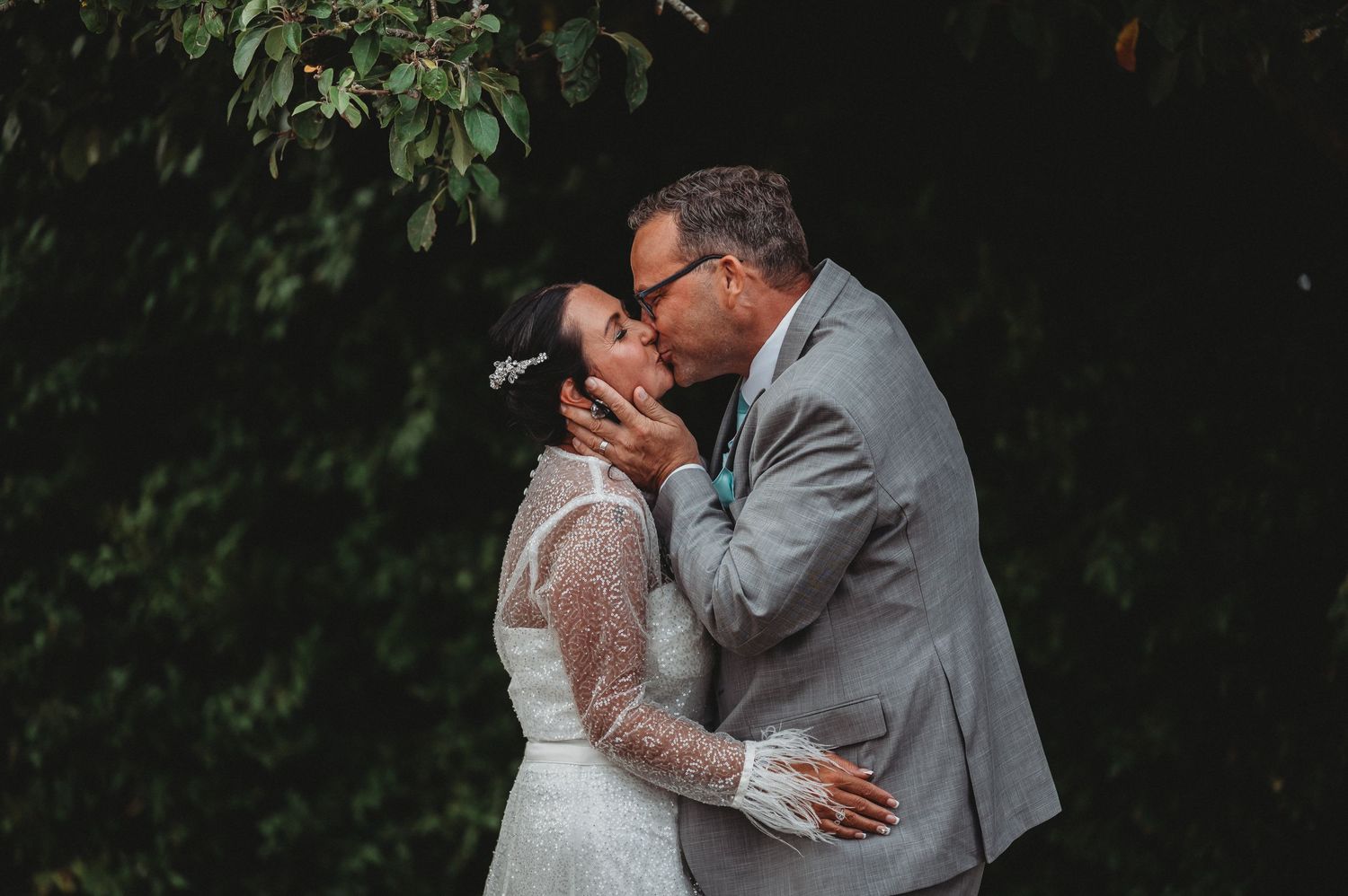 A romantic wedding couple shares an intimate kiss outdoors against a lush green garden backdrop.