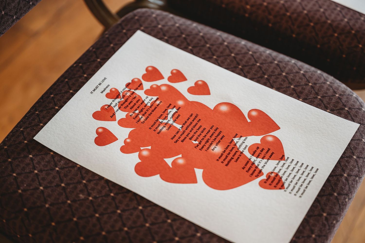 White paper with red heart designs and text layout on dark brown textured fabric background.