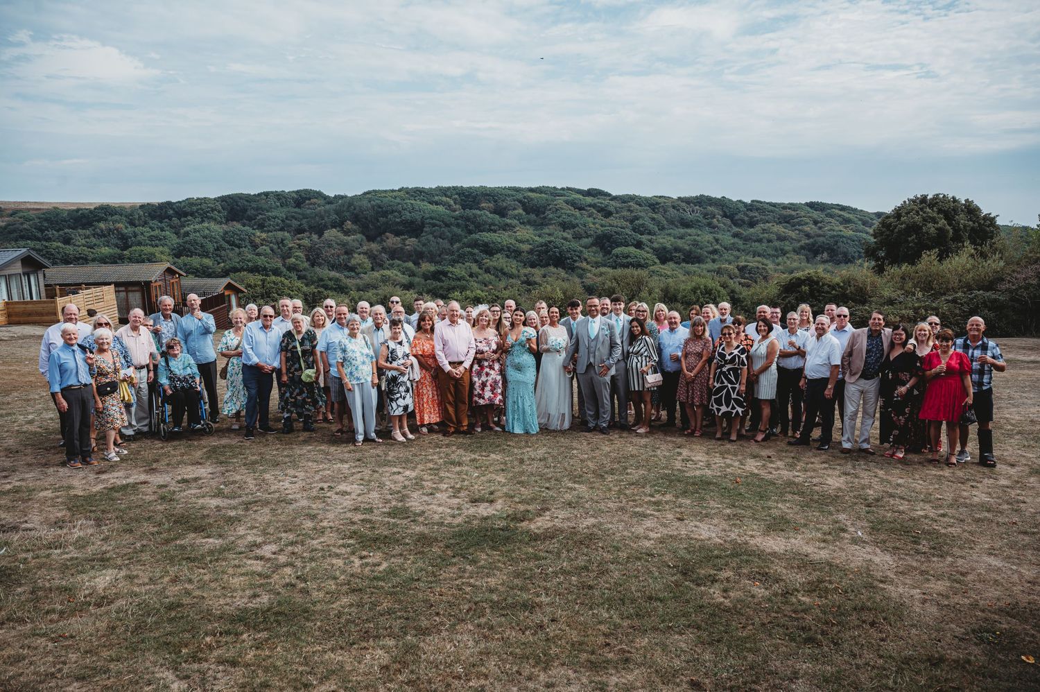 Large group of wedding guests gathered outdoors on a hilltop against a blue sky backdrop in summer.