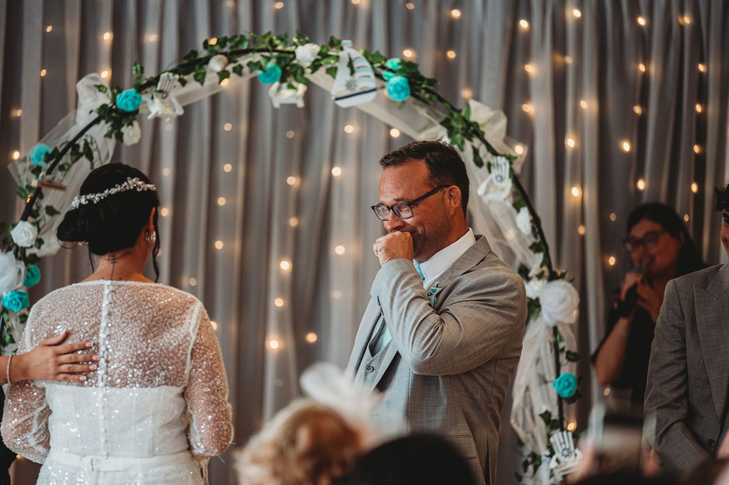 Wedding couple under a decorated arch with twinkle lights and turquoise accents.
