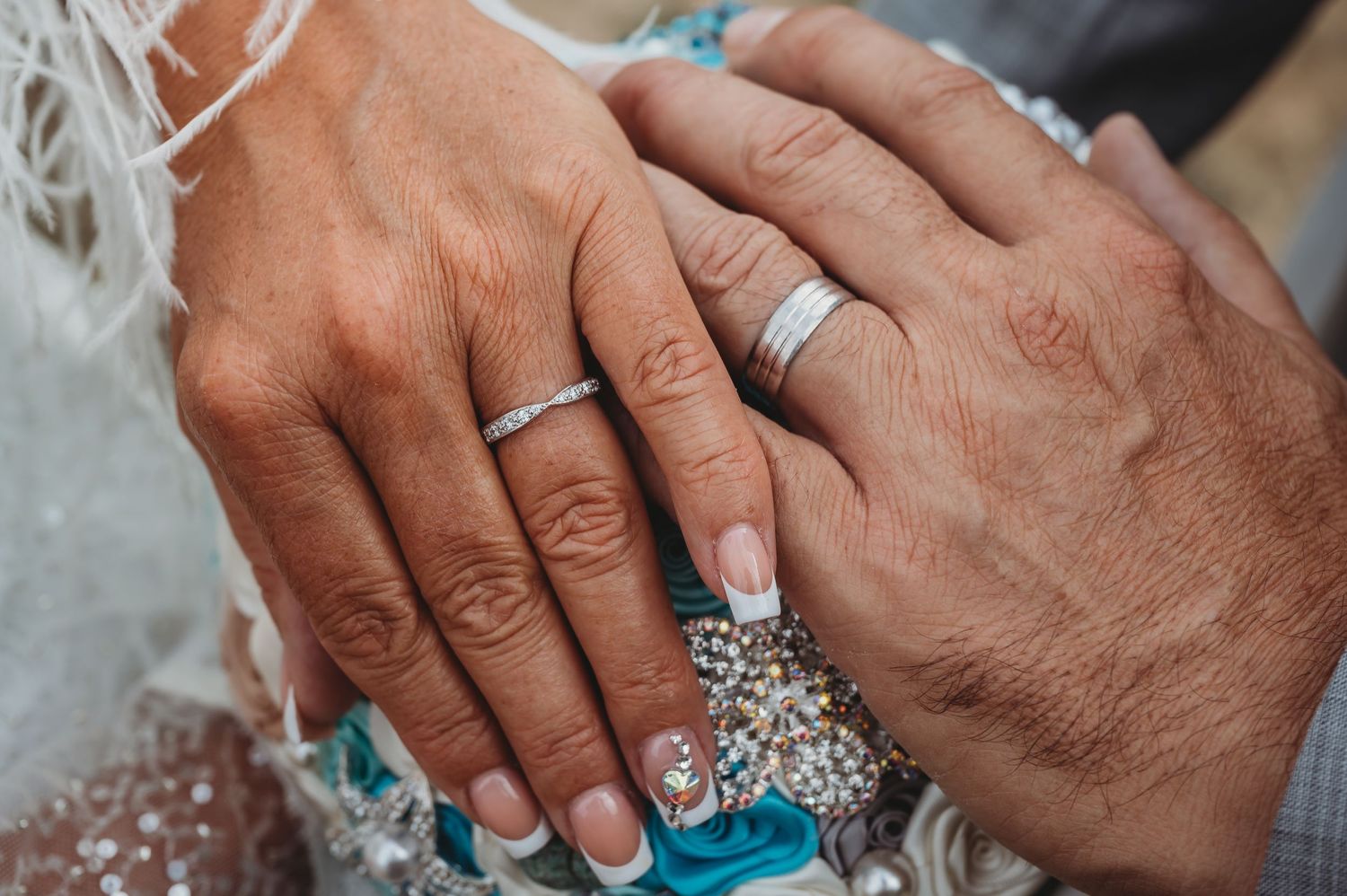 Close-up of wedding rings and jewelry on hands against a white lace background.