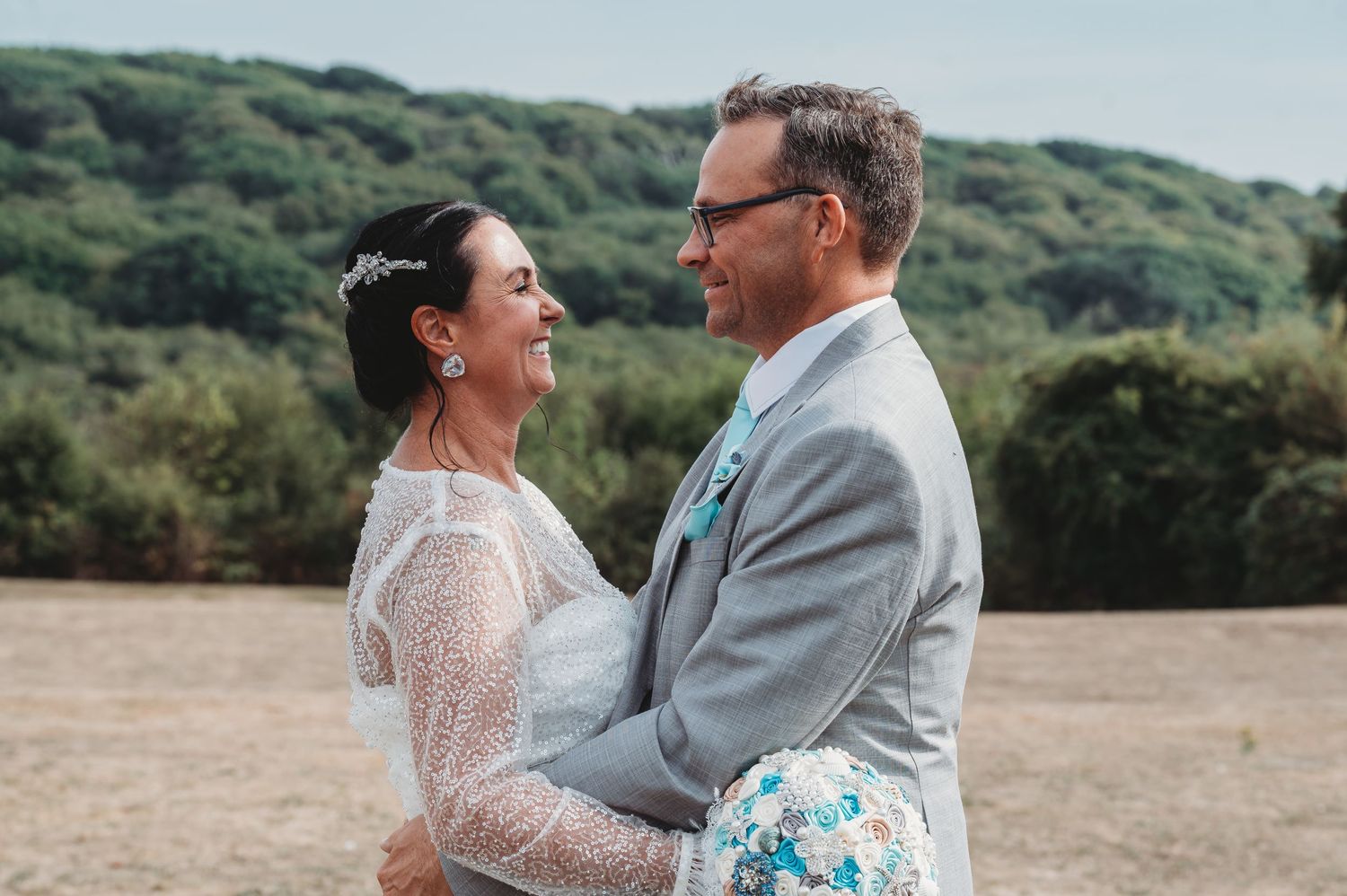 A romantic wedding couple sharing a tender moment outdoors with green hills in the background.