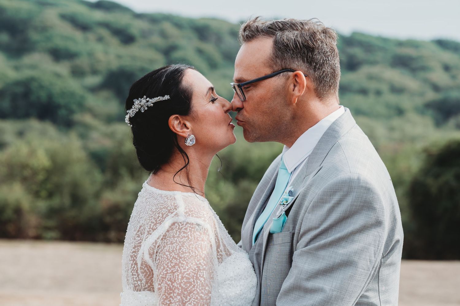A sweet wedding portrait showing an intimate moment between newlyweds against a scenic hillside backdrop.