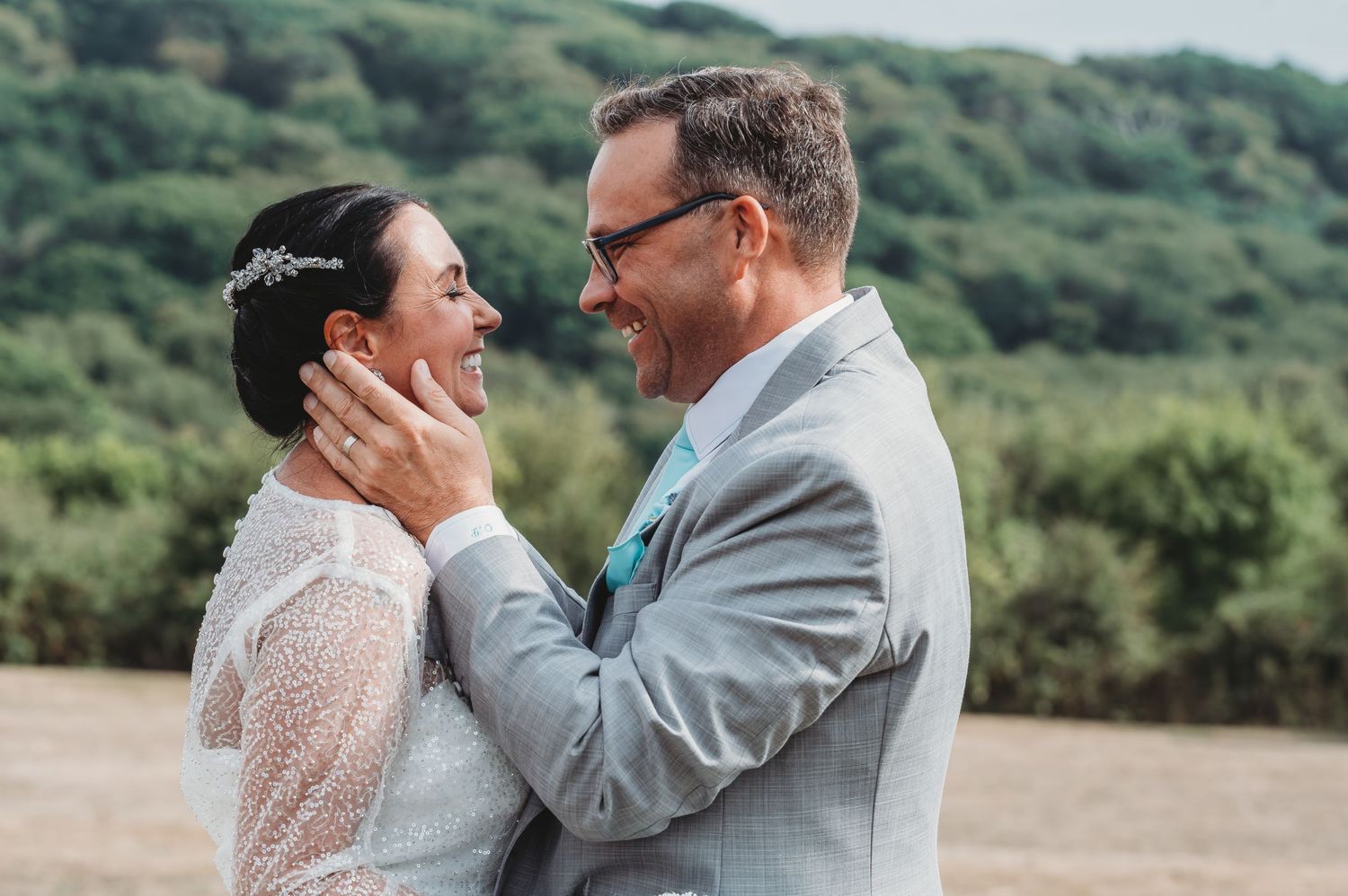 A tender moment between newlyweds outdoors with green hills in the background during a summer wedding.