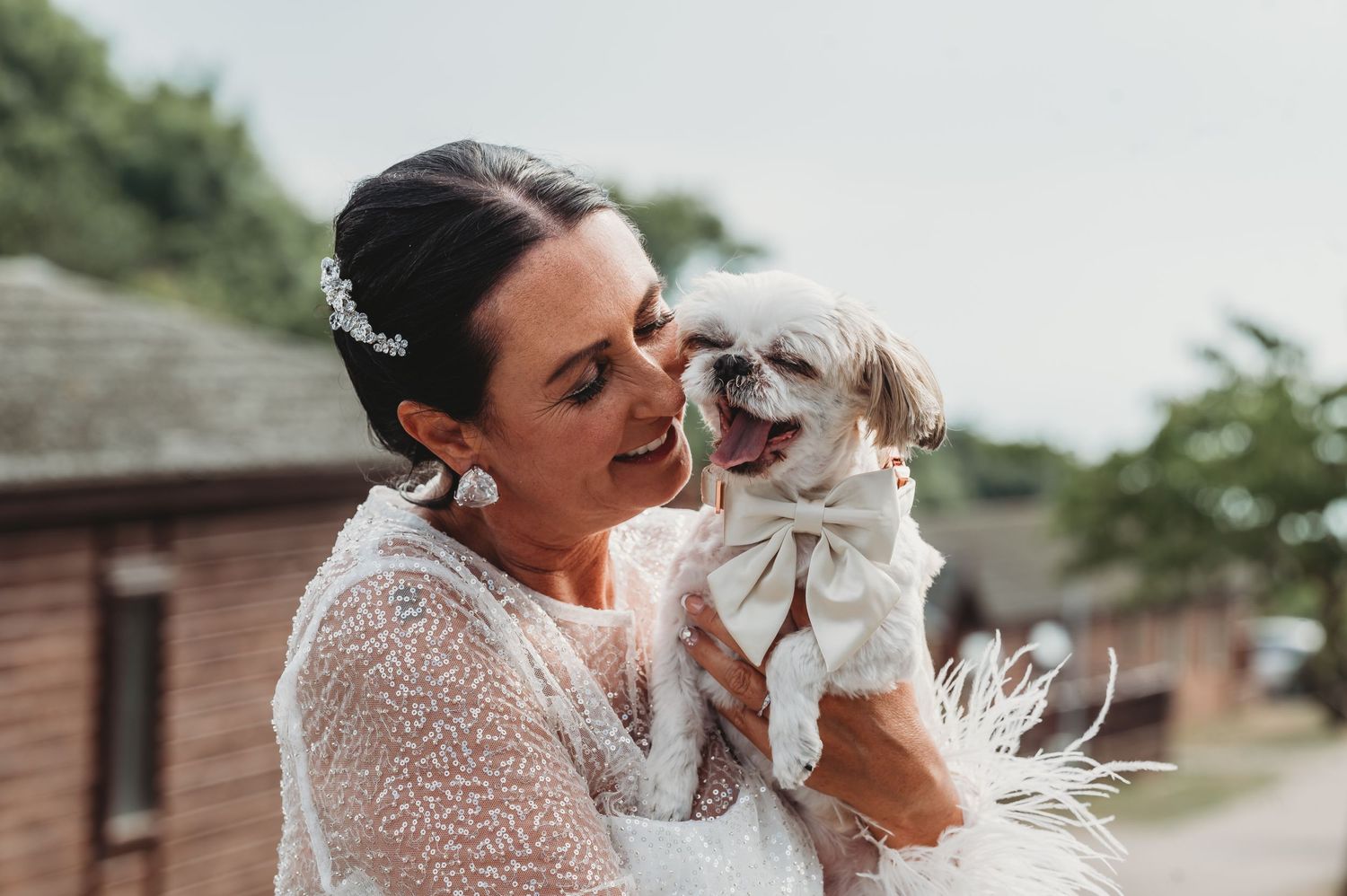 A person in a white lace dress shares a joyful moment with their small fluffy white dog outdoors.