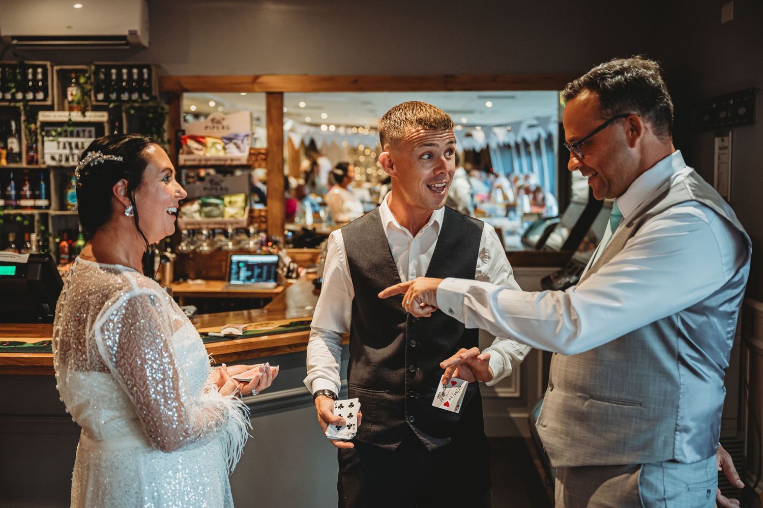 Three people conversing at a bar counter with drinks while celebrating in formal attire.