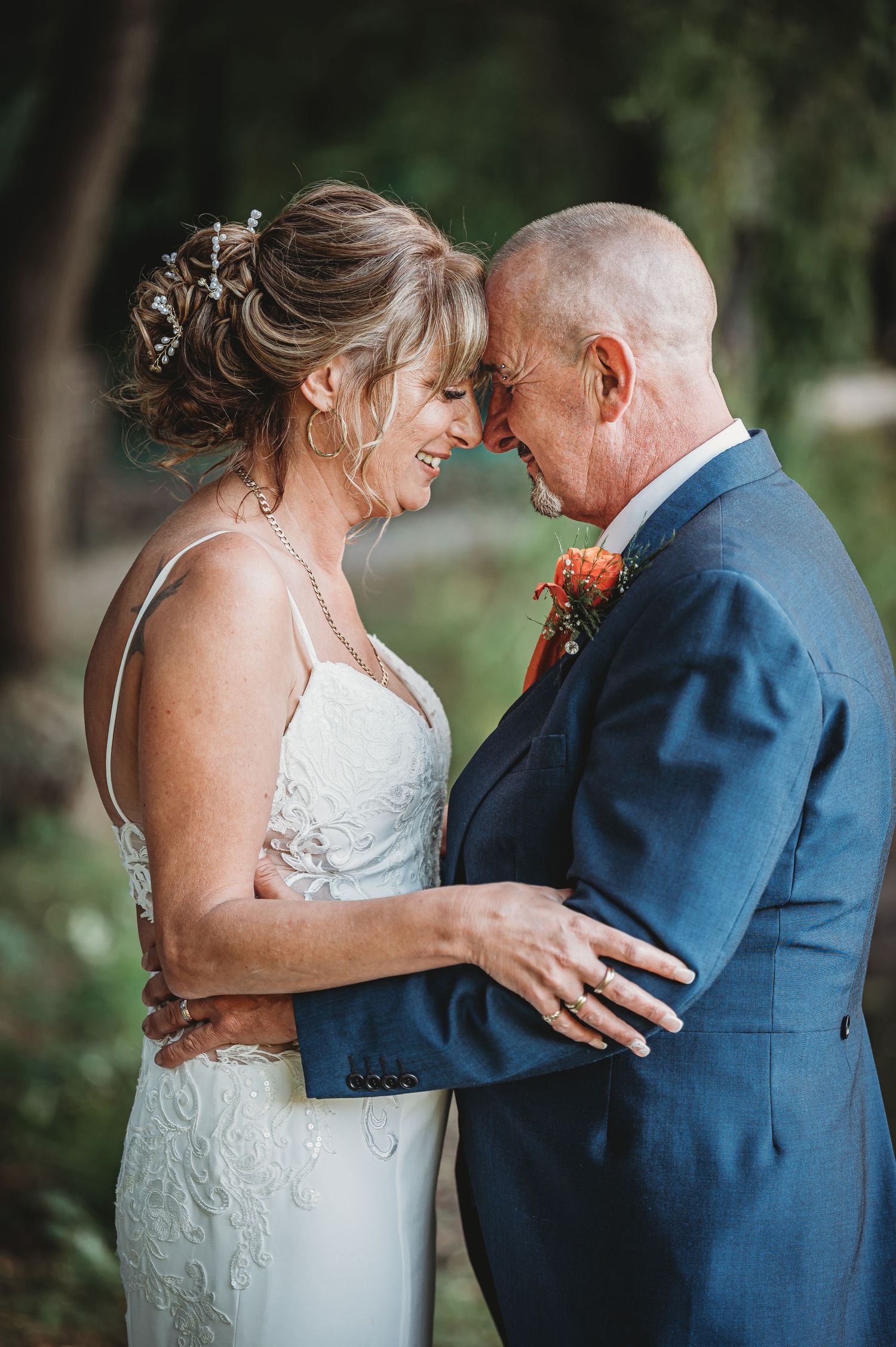 A tender moment between a bride in a white lace dress and groom in navy suit sharing an intimate embrace outdoors.