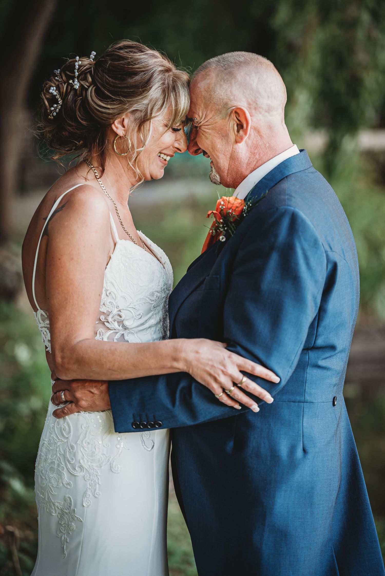 A tender moment between a bride in a lace gown and groom in navy suit sharing an intimate embrace outdoors.
