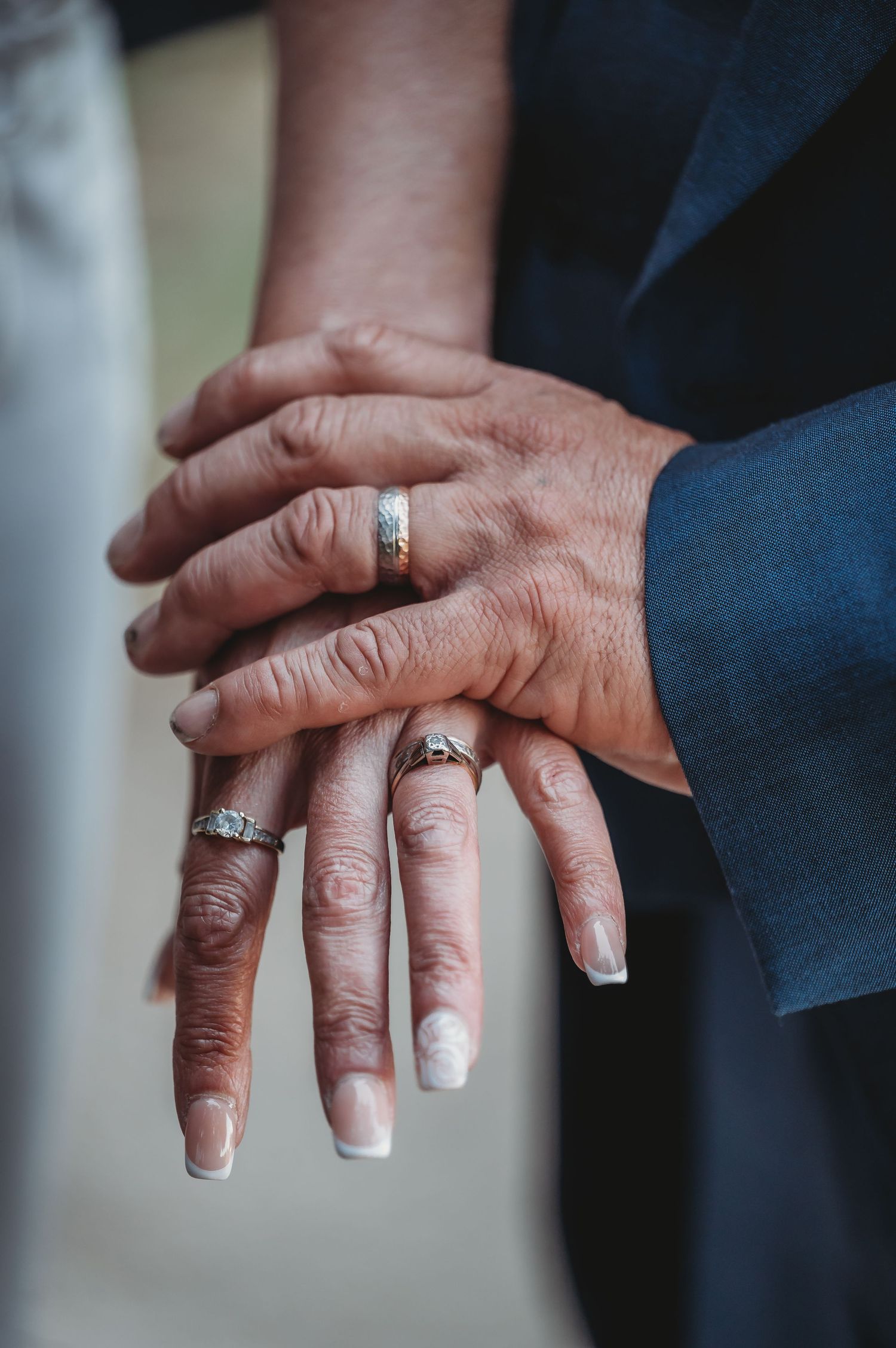 Close-up of hands displaying wedding rings with overlapping fingers and french manicured nails.