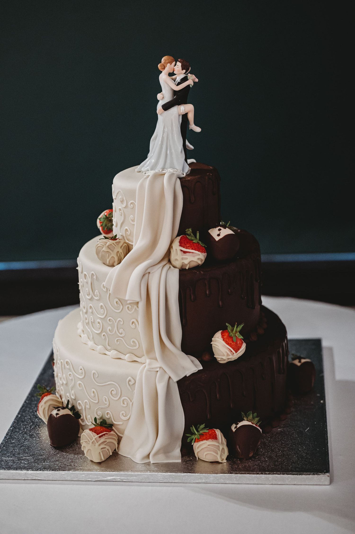 Creative wedding cake split in half with chocolate and vanilla tiers decorated with chocolate dipped strawberries and fondant draping.