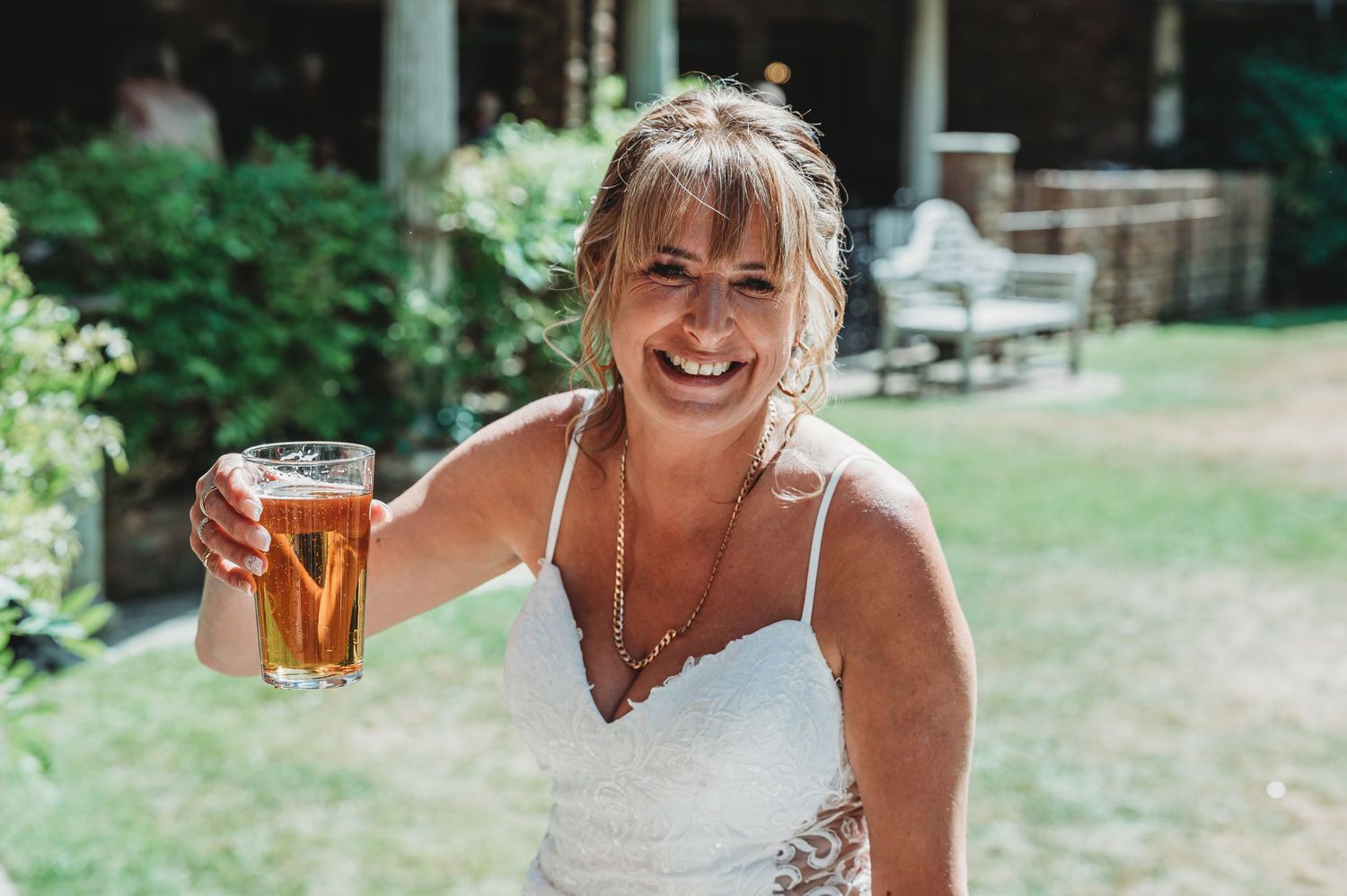 Person in a white dress holding up a beer glass while smiling and enjoying an outdoor summer celebration.