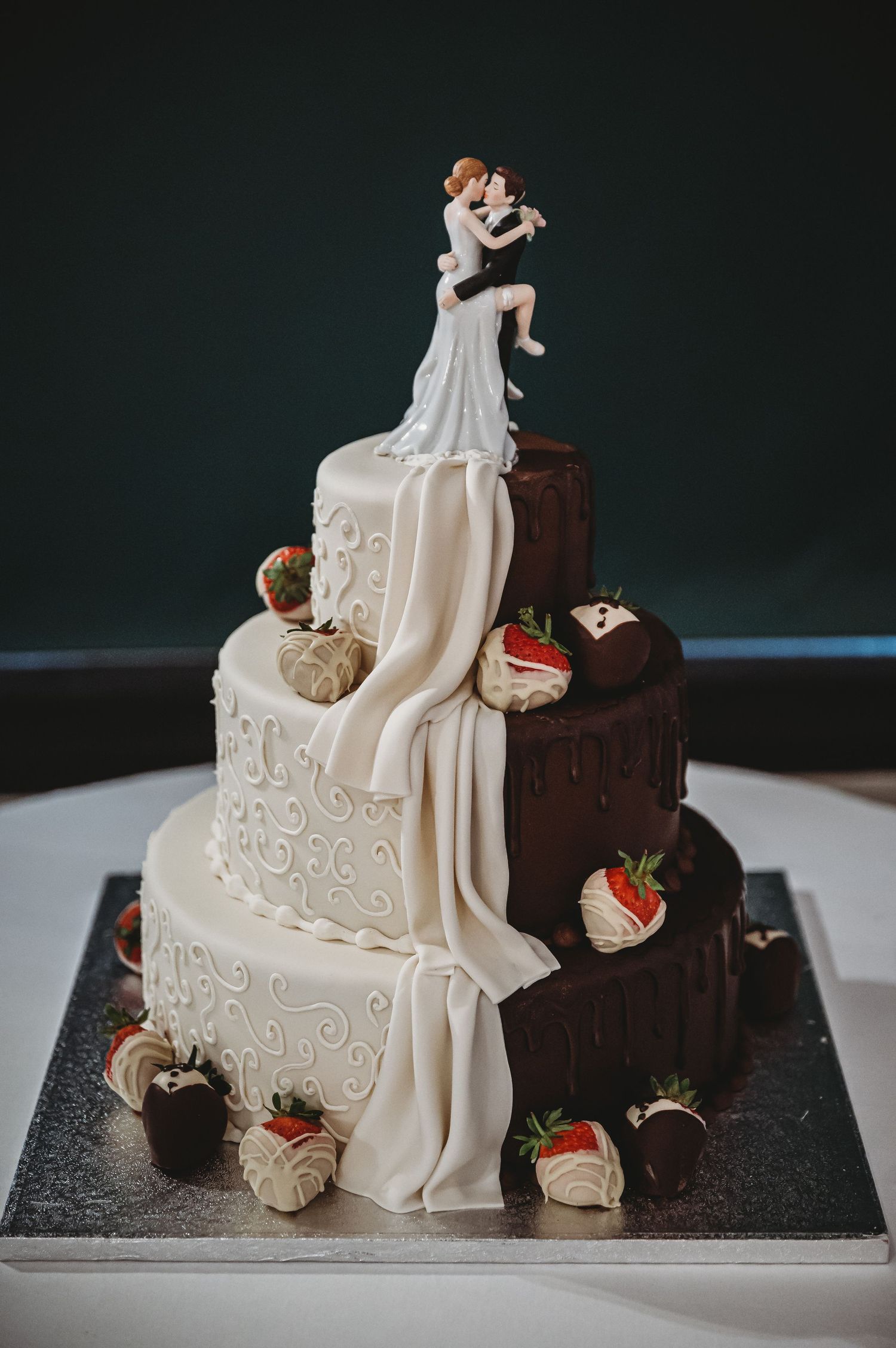 Creative two-tone wedding cake featuring half chocolate, half vanilla tiers with chocolate-dipped strawberries and a cake topper.