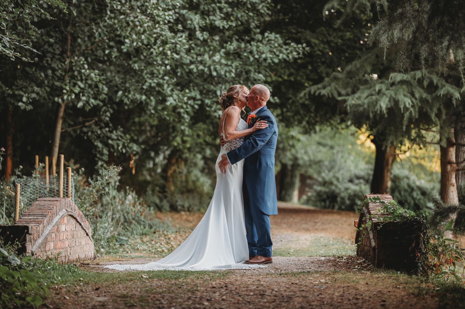 A couple embraces on a forest path surrounded by lush greenery during their wedding photoshoot.
